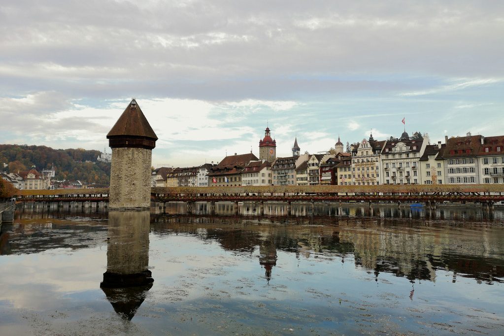The covered wooden bridge and octagonal stone water tower in Lucerne, with the old town frontage behind